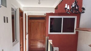 A narrow hallway with tiled flooring, a wooden door at the end, and a balcony with a railing and potted plants. - Hotel El Portal Sololateco (Sololá)