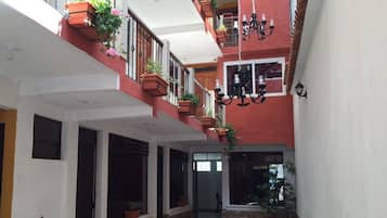 Un patio estrecho con un edificio rojo, paredes blancas y varios balcones con plantas en macetas.