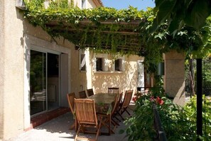 Une terrasse extérieure avec une table et des chaises, entourée d’une pergola recouverte de verdure.