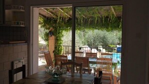A dining area with a table set for two, a view of a pool and outdoor seating, and a brick wall on one side. - Spacious, pleasant house in the heart of a Provencal village (Le Pin)