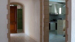 A hallway with tiled flooring and stone arches leading to a room with a green door. - Spacious, pleasant house in the heart of a Provencal village (Le Pin)