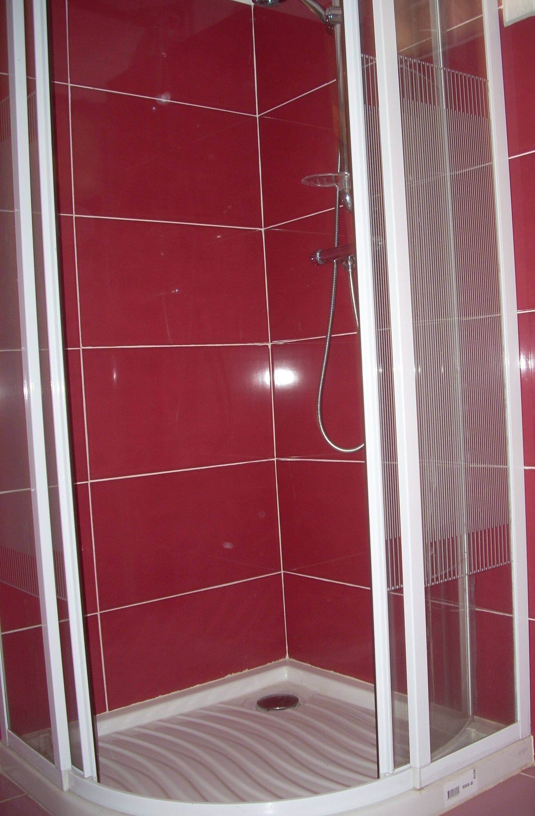 A shower enclosure with red tiles and a white frame.