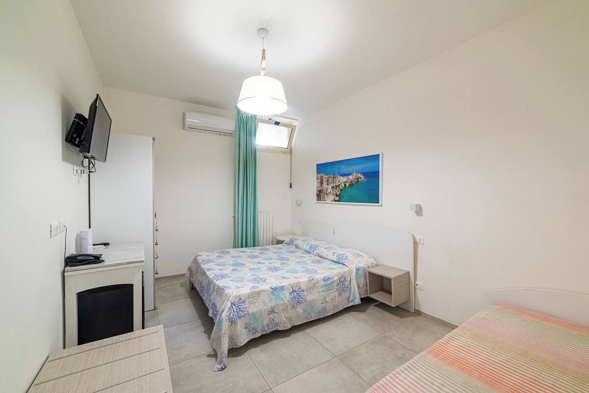 Une chambre à coucher avec un lit, un bureau, une télévision et une fenêtre avec des rideaux.