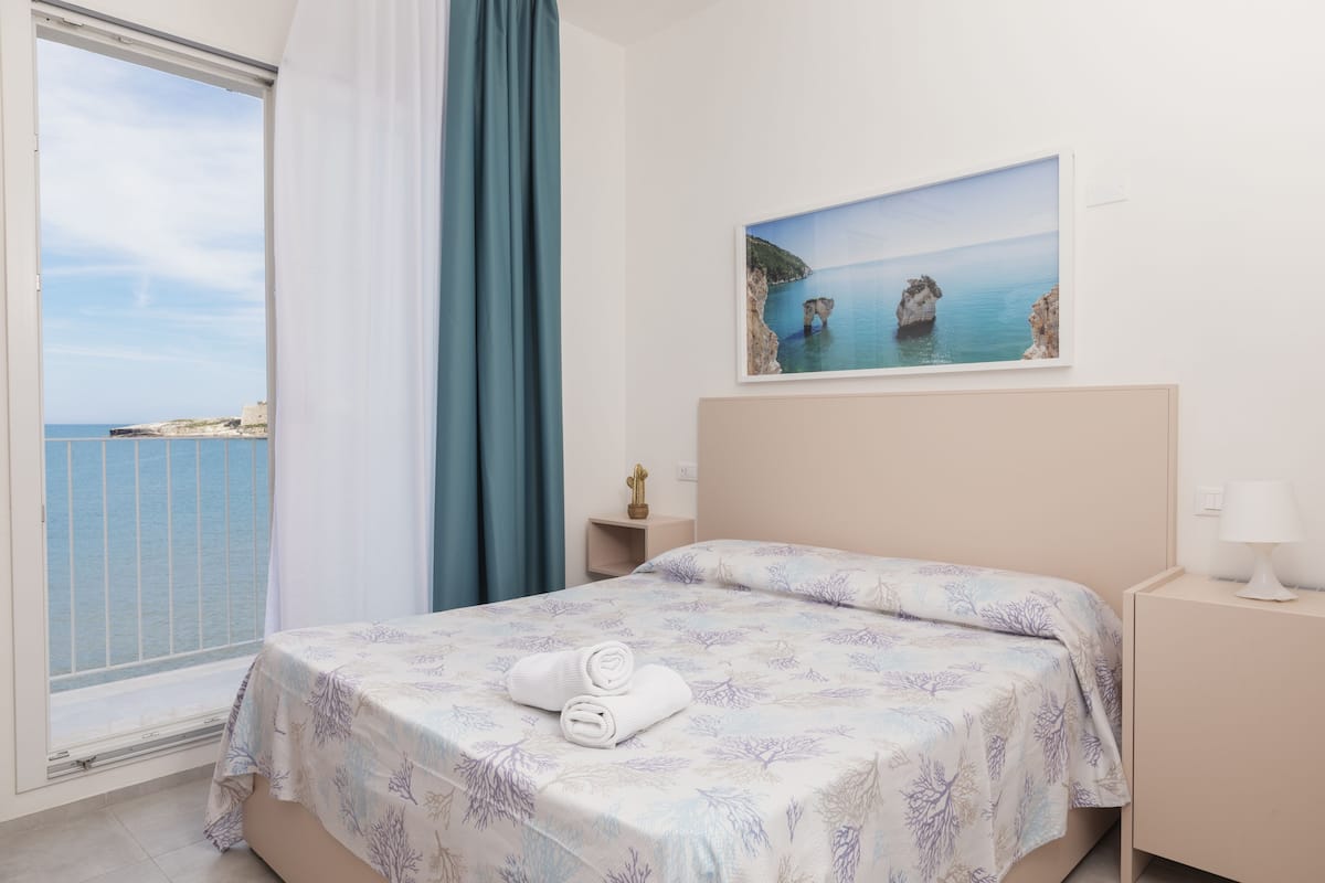 Une chambre à coucher avec un lit, une table de chevet, un tableau et une vue sur la mer.