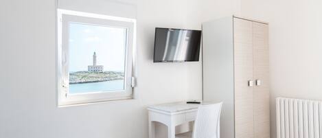 A bedroom with a bed, a desk with a chair, a wardrobe, a TV, and a window with a view of a building.