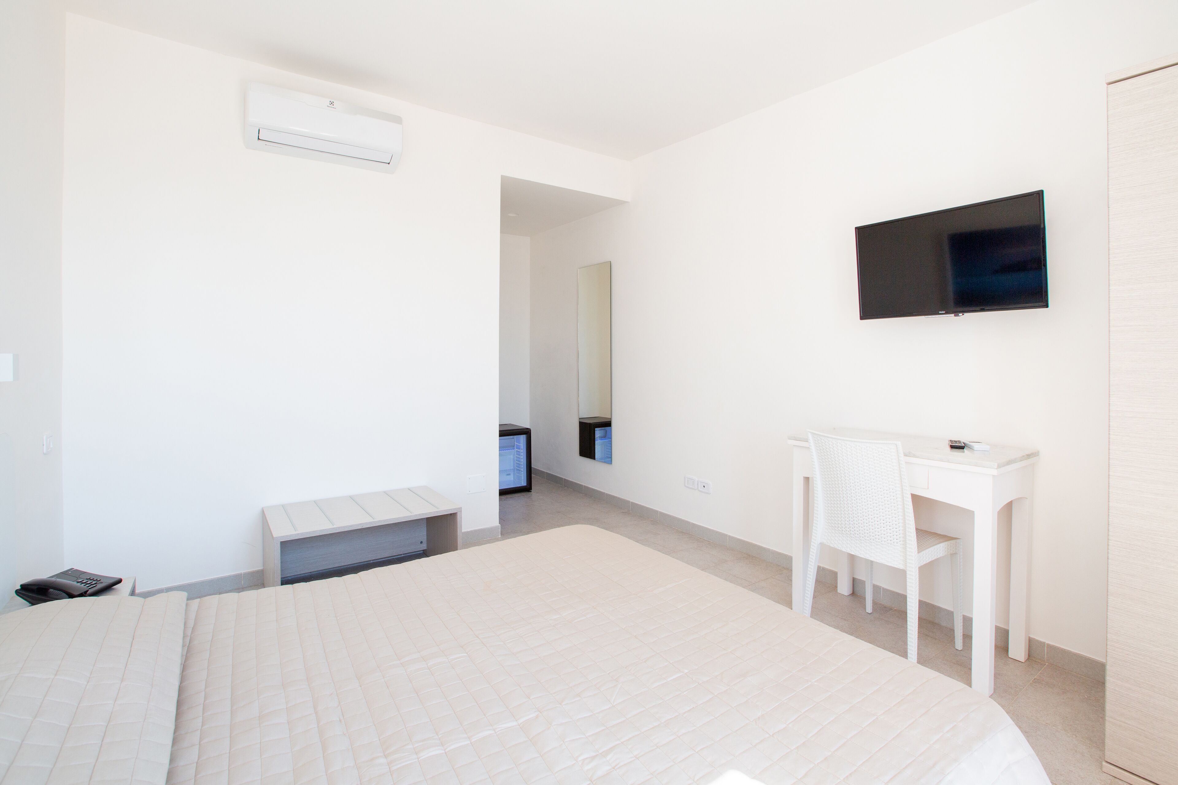 Una habitación de hotel moderna con una cama grande, un escritorio con silla, un televisor de pantalla plana y un espejo.