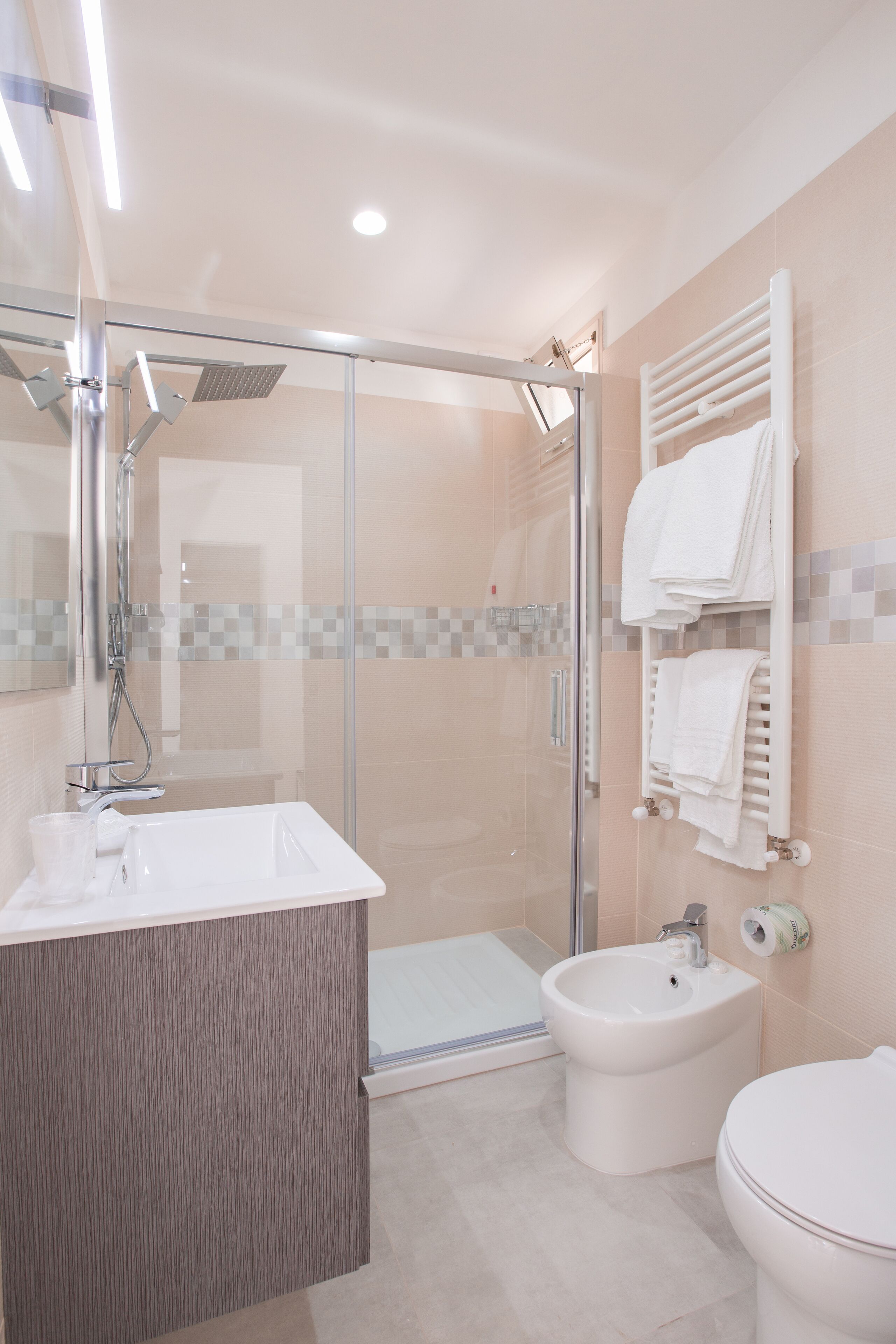 Un baño moderno con ducha de vidrio, tocador con espejo, un bidé y un inodoro.