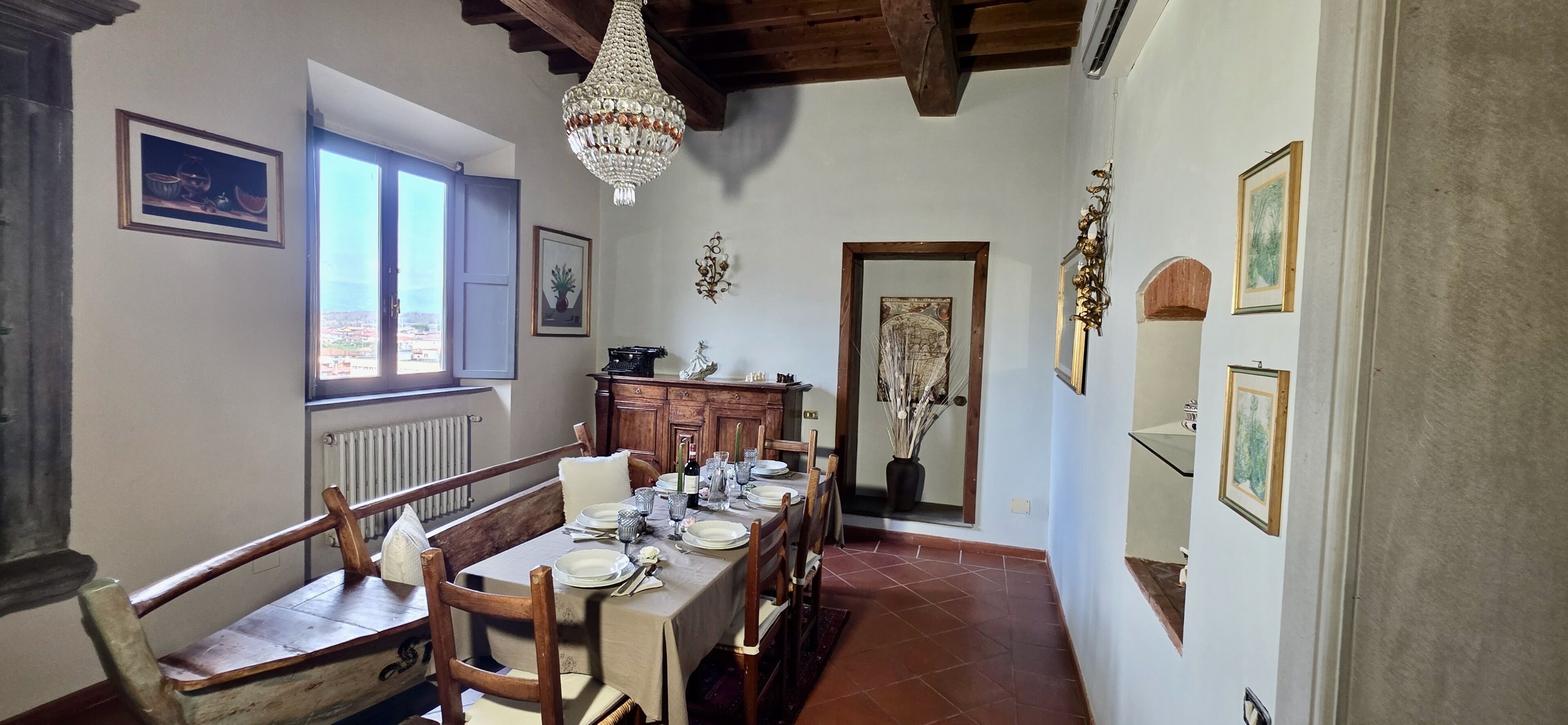 A dining area with a table set for four, wooden chairs, a chandelier, and artwork on the walls.