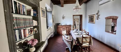 A dining area with a table set for four, a bookshelf with books, a chandelier, and a wooden cabinet.