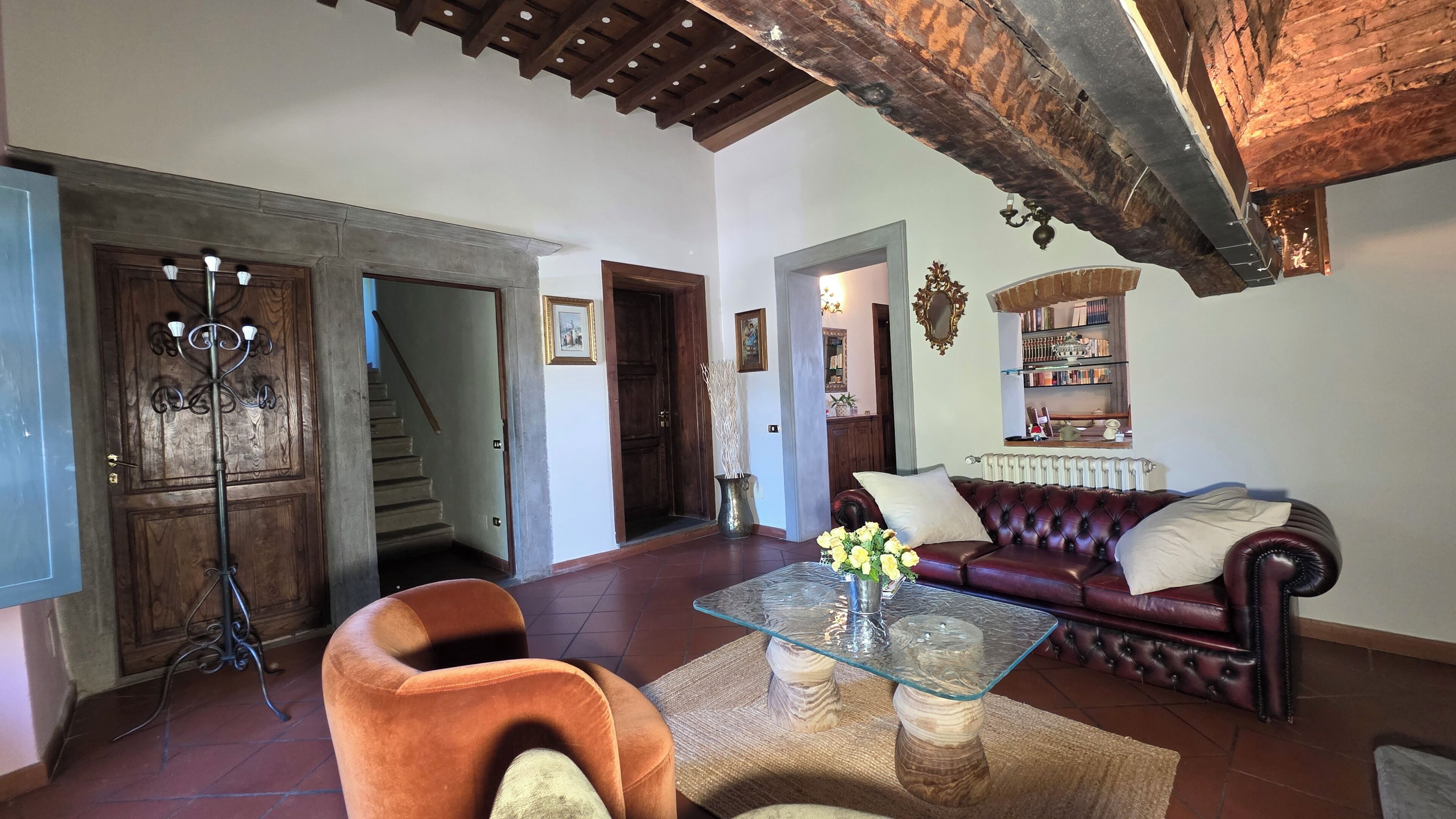 A living room with a glass coffee table, a leather sofa, a wooden floor, and a staircase leading to another room.