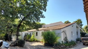 Un bâtiment blanc avec un toit en tuiles, entouré d’arbres et d’un chemin de gravier.