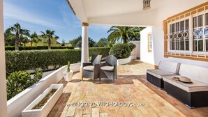 A covered patio with wicker furniture, a view of the garden, and a website URL.