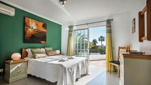 A bedroom with a bed, a nightstand, a desk, and a view of the outdoors.