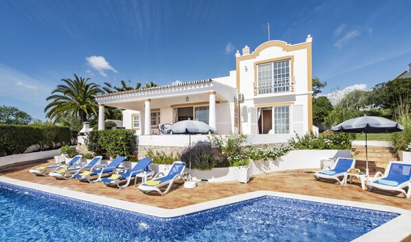 Een villa met een zwembad, ligbedden en een overdekt terras.