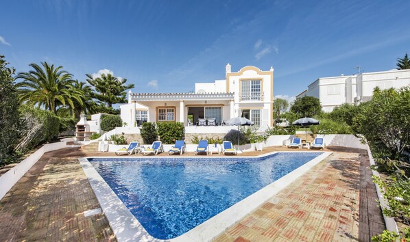 A villa with a swimming pool, lounge chairs, and a patio area.