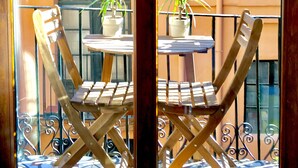 Une chaise et une table en bois sur un balcon doté de rampes en métal et de plantes en pot.