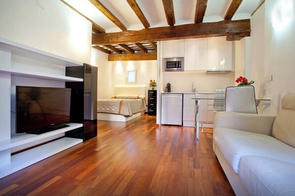 A modern living room with a flat-screen TV, a sofa, a dining area with a glass table, and a kitchen with a microwave. - Sun Studio @ Valencia - Excellent - with Balcony :) City Center (Valencia)