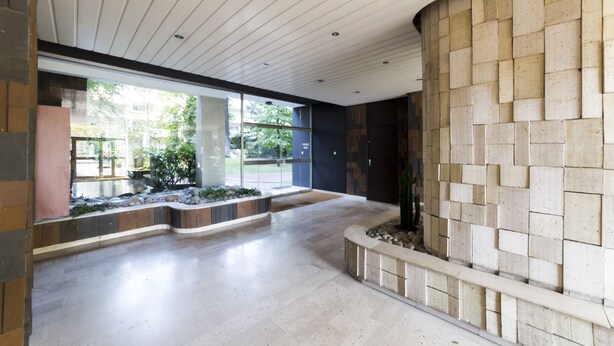 Un hall d’entrée spacieux, doté d’un banc incurvé, d’un mur en pierre et d’une grande fenêtre donnant sur un paysage verdoyant.