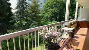 Un balcon avec une table et des chaises en bois, entouré de plantes en pot et agrémenté d’une balustrade blanche.