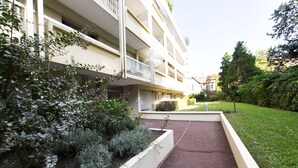 Un immeuble à plusieurs étages doté de balcons, d’un jardin aménagé et d’un chemin pavé.