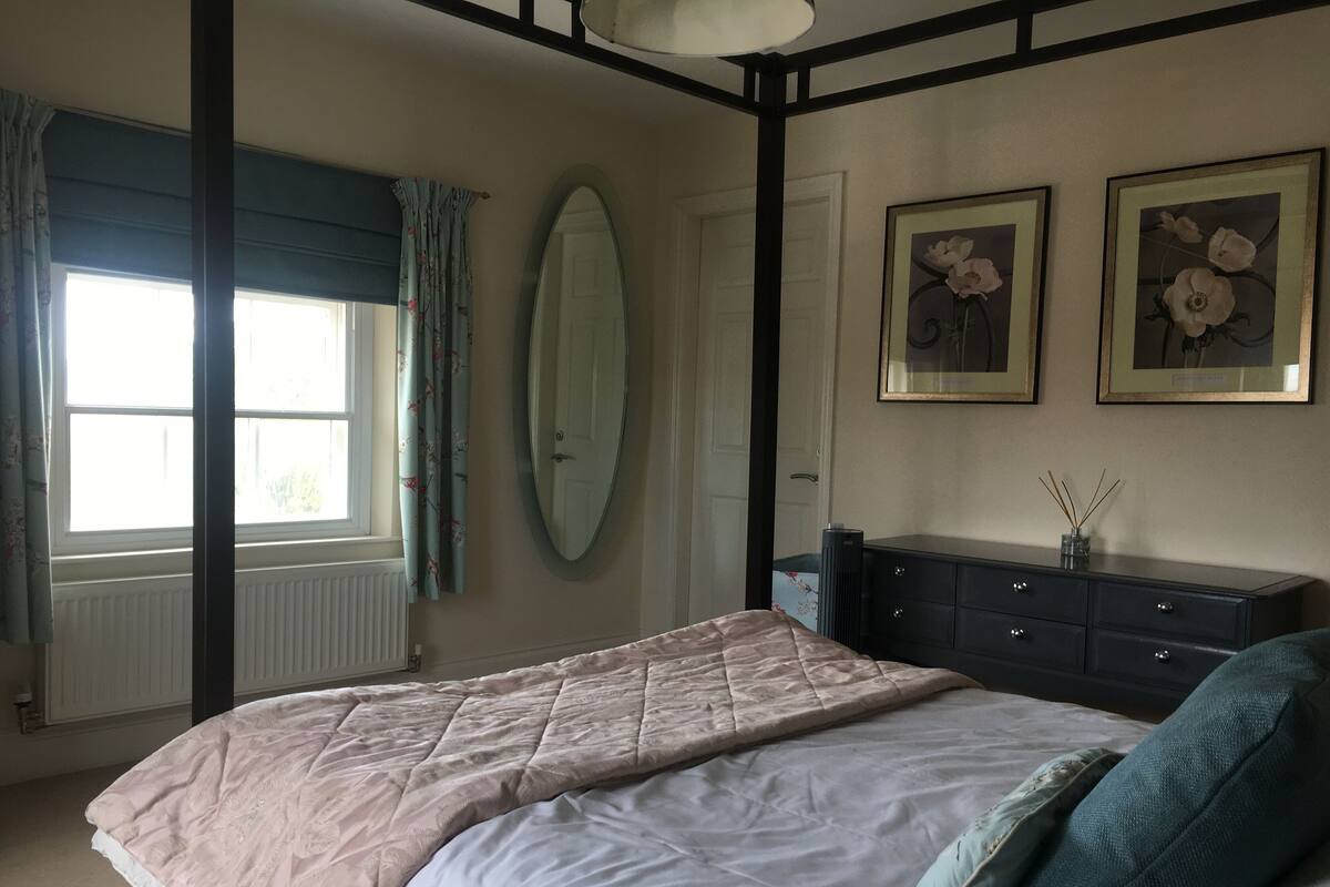 Une chambre à coucher comprenant un lit, une commode, un miroir et deux tableaux floraux encadrés accrochés au mur.