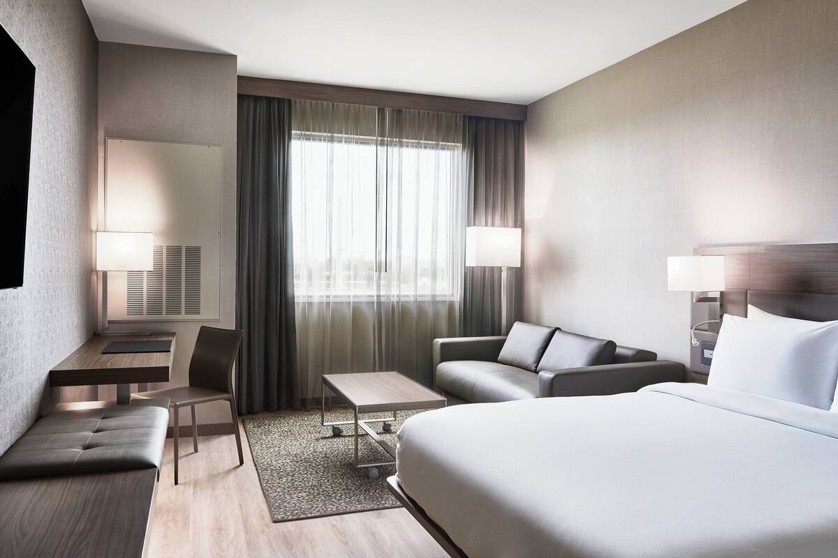 A modern hotel room with a bed, a sofa, a desk, and a chair.