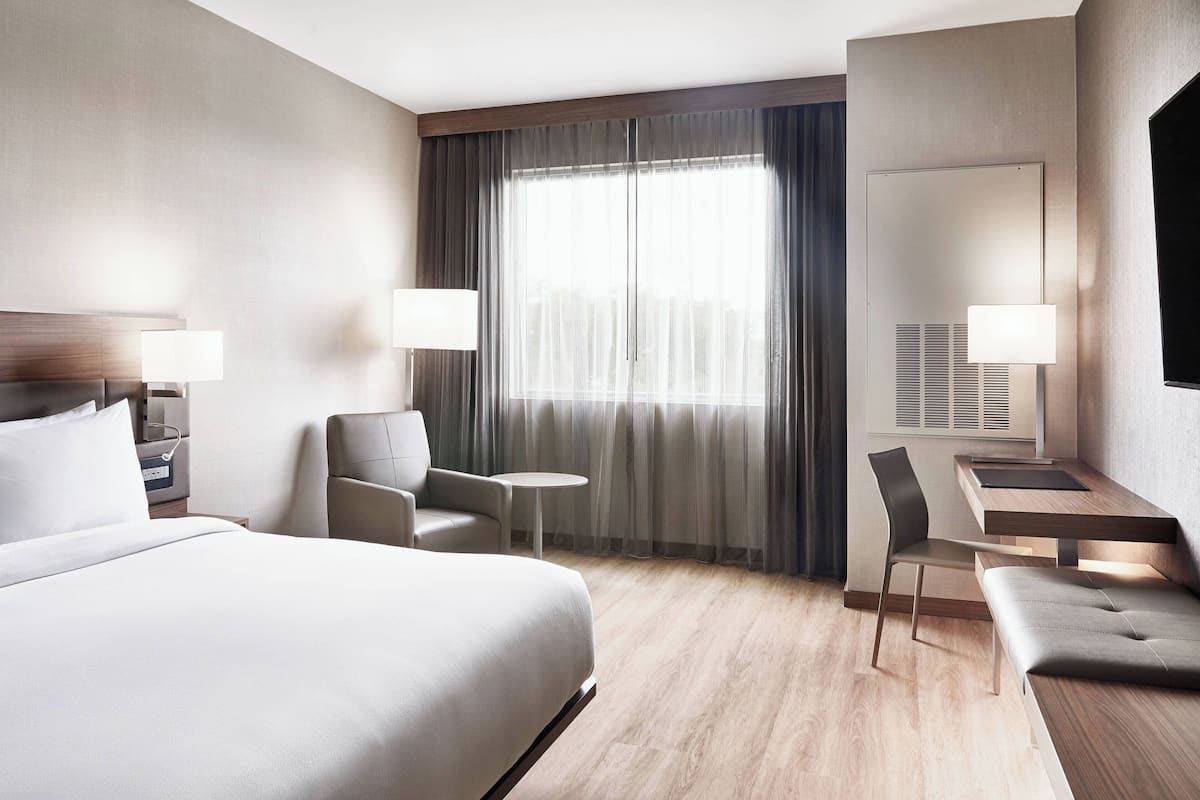 A modern hotel room with a large bed, a desk, a chair, and a small table.