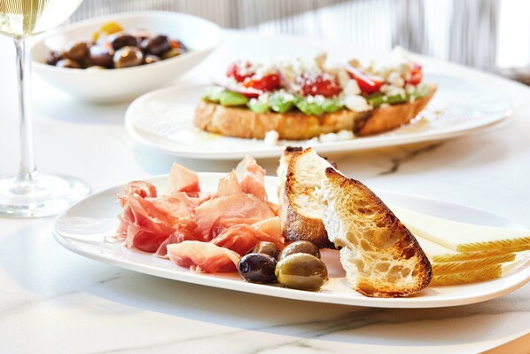Una mesa con platos de comida, incluyendo jamón serrano, aceitunas y pan.