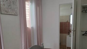 A bedroom with two single beds, a bathroom visible through an open door, and a shower area.