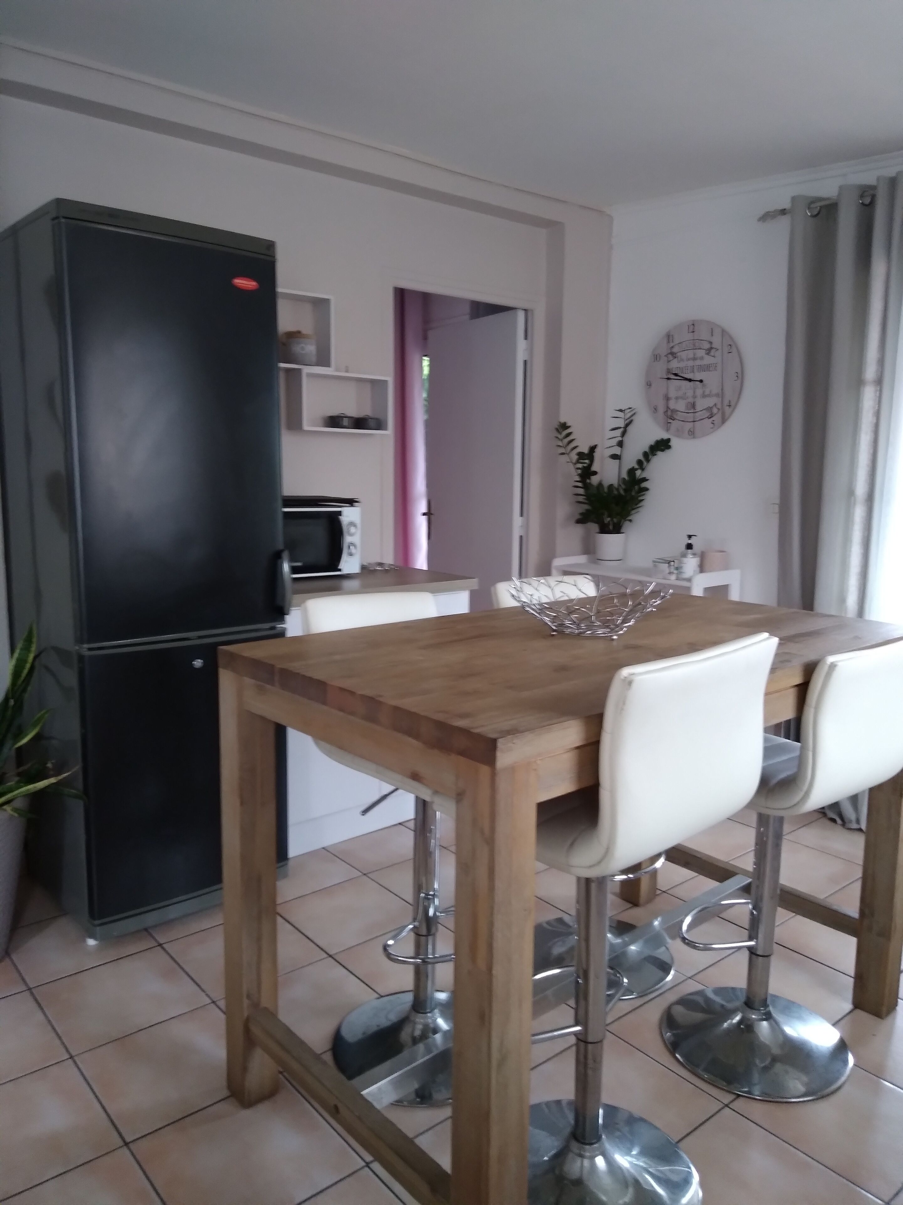 A modern kitchen with a black refrigerator, a microwave, and a wooden dining table with white chairs.