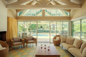 A spacious living area with a large glass door leading to a pool, wicker furniture, and a wooden coffee table.