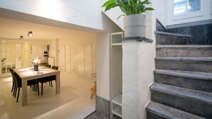 A dining area with a wooden table and chairs, a potted plant, and a staircase with a textured wall. - Saint Pauls Suite 1 (Antwerp)