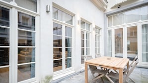 A patio area with a wooden table and chairs, large windows, and a view of the interior. - Saint Pauls Suite 1 (Antwerp)