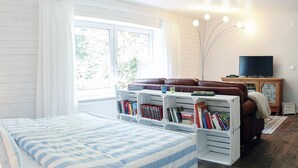 Une pièce confortable avec un lit, un canapé en cuir marron, une télévision et une bibliothèque remplie de livres.