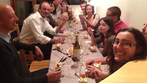 Eine Gruppe von Menschen sitzt an einem Tisch mit Essen und Getränken, was auf ein Treffen oder eine Mahlzeit hindeutet.
