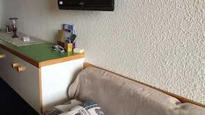 Ein Zimmer mit einem grünen Schreibtisch, einem Wand-Fernseher, einer Couch und einer strukturierten Wand.
