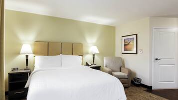 Una habitación de hotel con una cama grande, dos lámparas de noche, una silla, una mesita y una puerta.