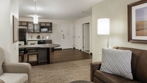 A modern living room with a brown sofa, a dining area with a round table, and a kitchen in the background. - Candlewood Suites Brighton by IHG (Brighton)
