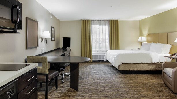 A hotel room with a bed, a desk with a chair, a television, and a window with curtains. - Candlewood Suites Brighton by IHG (Brighton)