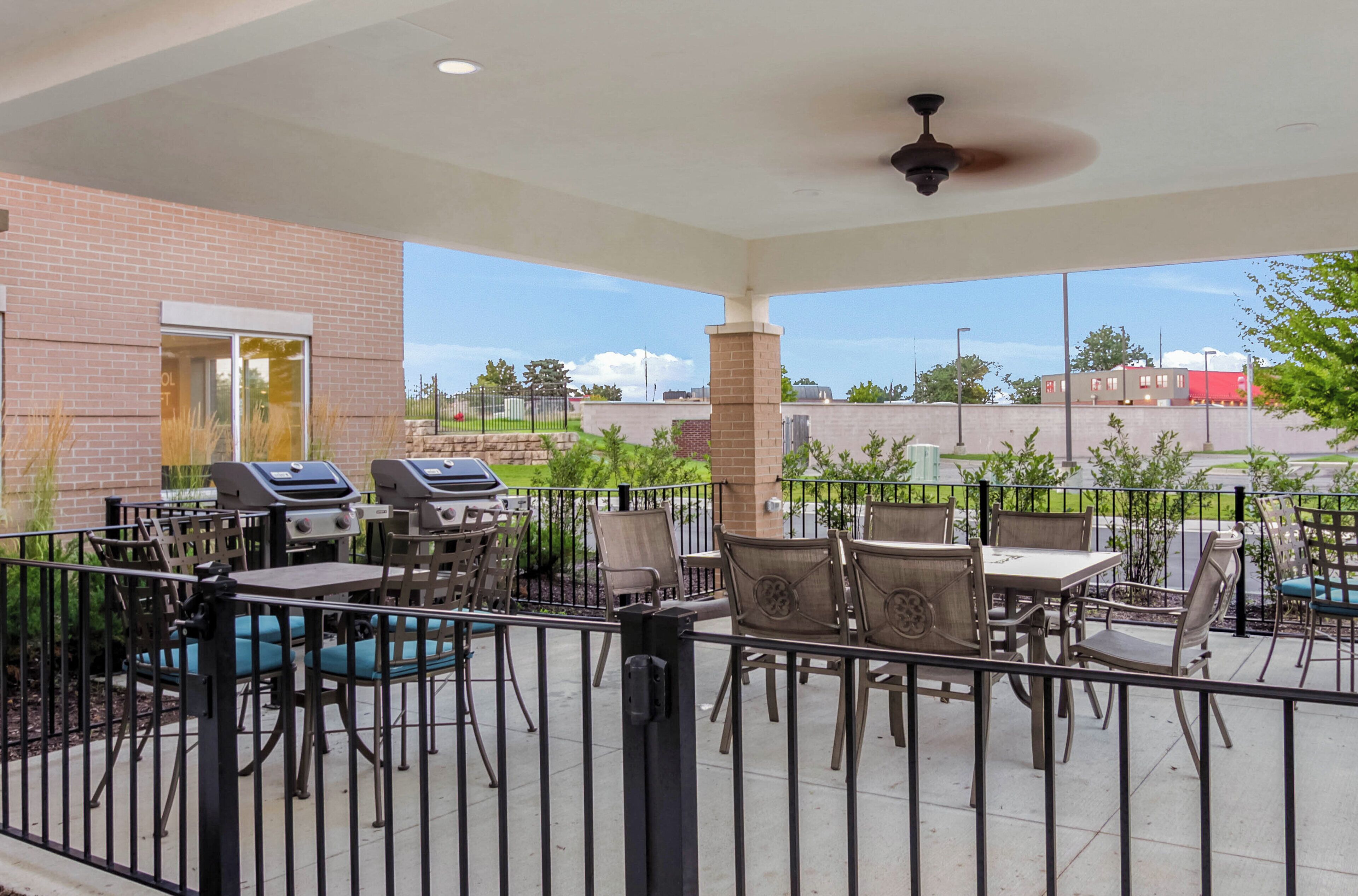 An outdoor patio area with barbecue grills, tables, and chairs, enclosed by a metal fence.