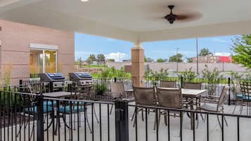 An outdoor patio area with barbecue grills, tables, and chairs, enclosed by a metal fence.