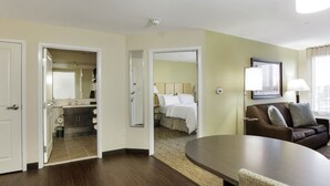 A hotel room with a large bed, a sitting area with a couch and a table, and a bathroom visible through an open door. - Candlewood Suites Brighton by IHG (Brighton)