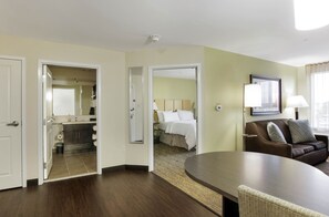 A hotel room with a large bed, a sitting area with a couch and a table, and a bathroom visible through an open door. - Candlewood Suites Brighton by IHG (Brighton)