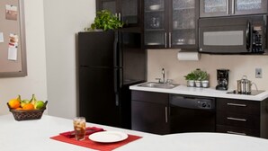 A modern kitchen with a black refrigerator, a microwave, and a sink. There is a fruit basket and a glass of iced tea on the counter. - Candlewood Suites Brighton by IHG (Brighton)