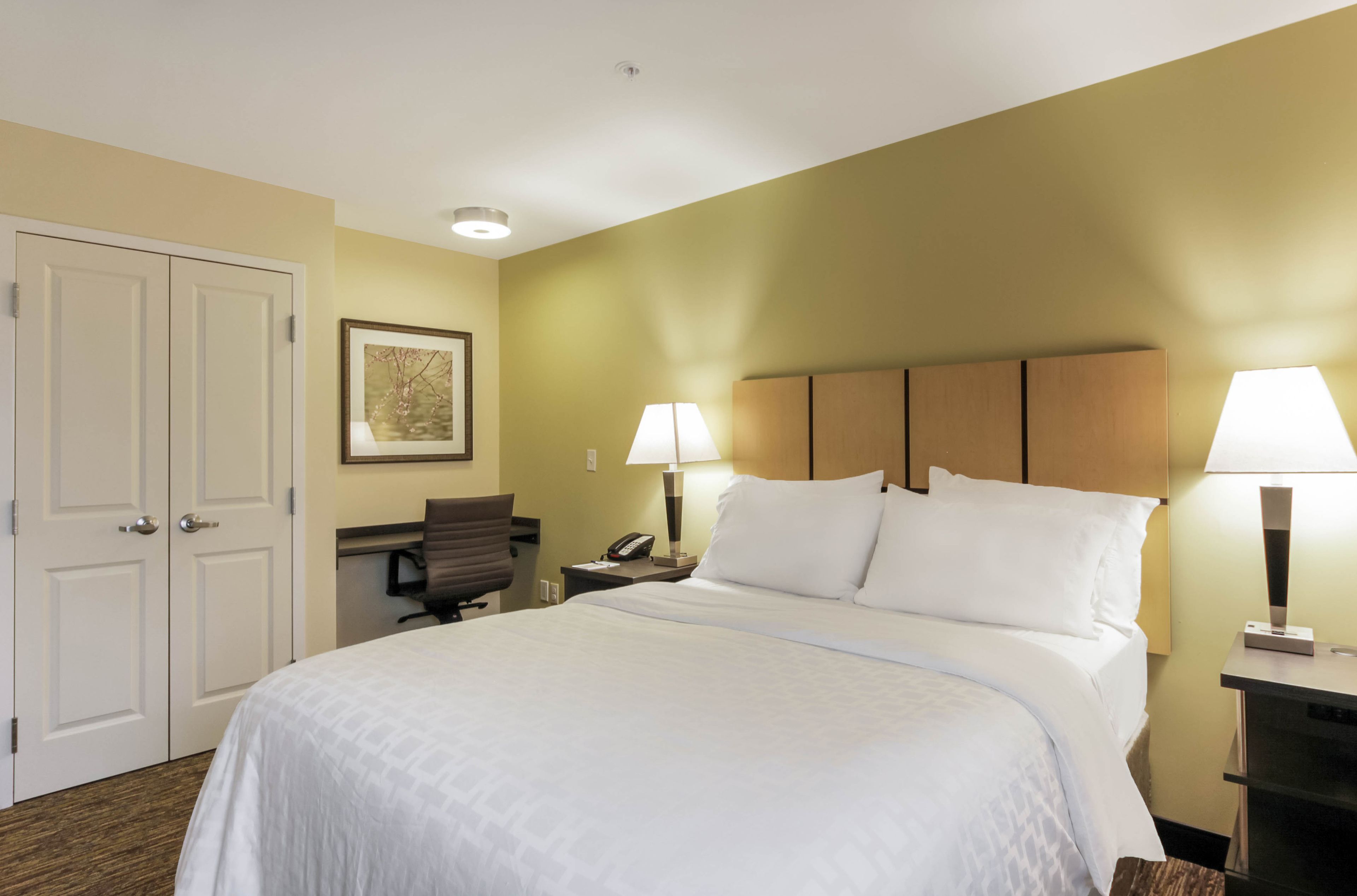 A hotel room with a large bed, two bedside lamps, a desk with a chair, and a door.