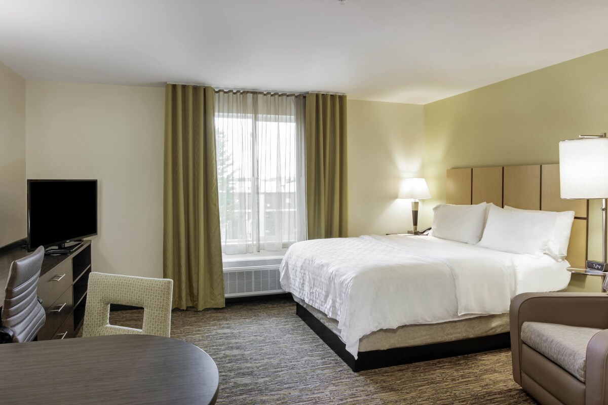 A hotel room with a bed, a desk with a TV, a chair, and a lamp.