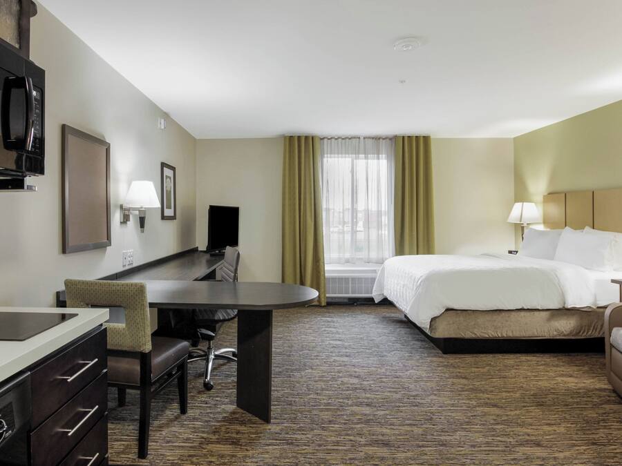 Ein Hotelzimmer mit Bett, Schreibtisch, Stuhl, Fernseher und einem fensterbepflanzten Fenster.