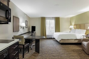 A hotel room with a bed, a desk, a chair, a television, and a window with curtains. - Candlewood Suites Brighton by IHG (Brighton)
