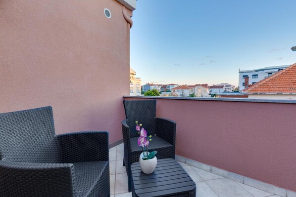 A balcony with wicker furniture and a small table, a potted plant, and a view of the cityscape. - Hotel Marinko (Zadar)