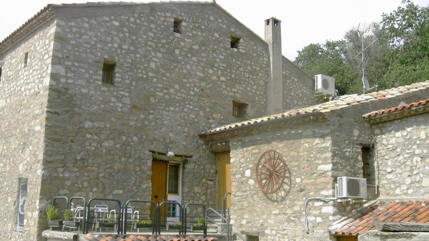 A stone building with a wooden door, a small balcony with metal railings, and an air conditioning unit mounted on the wall. - Albergue Rural Cal Picarol (Camarasa)